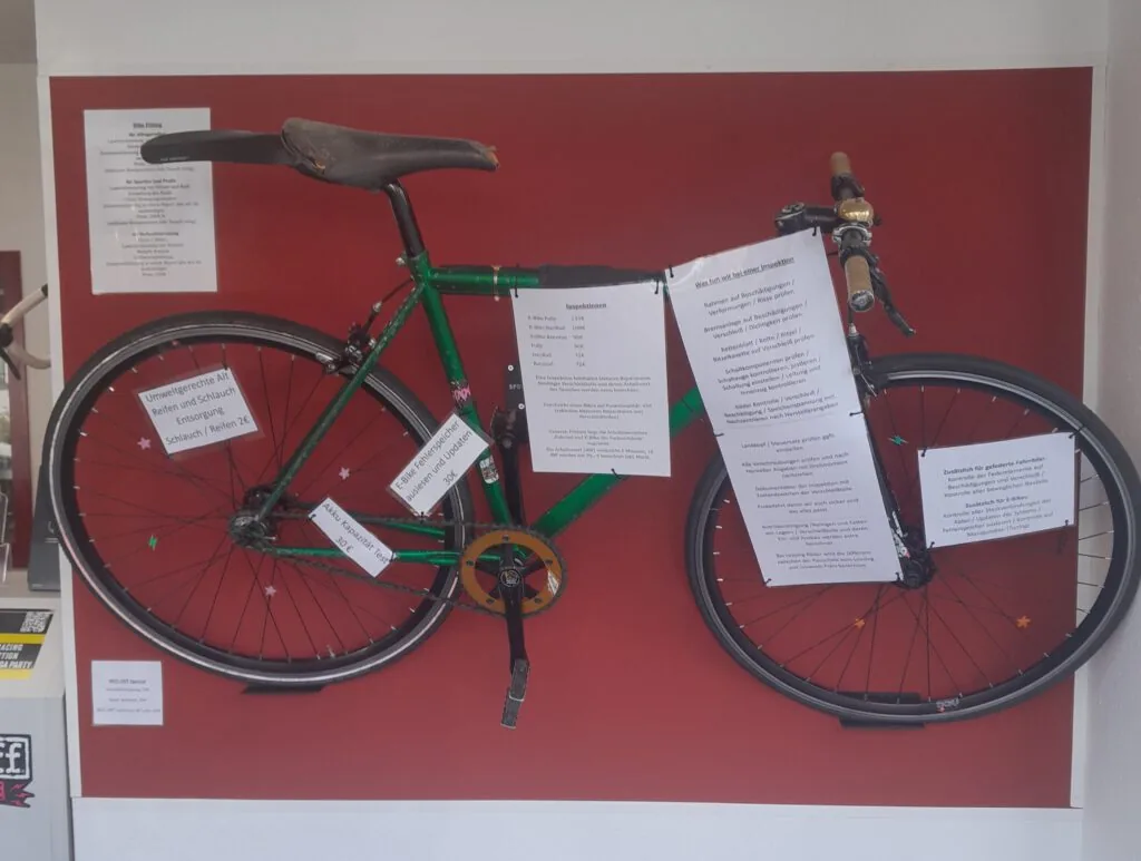 Grünes Rennrad an einer roten Wand, daneben Infozettel zu Inspektionen und Preisen